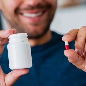 A man holding a supplement container and a pill