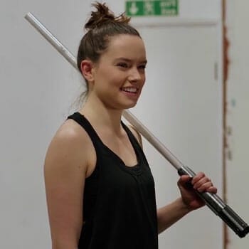 daisy ridley smiling while holding a lightsaber