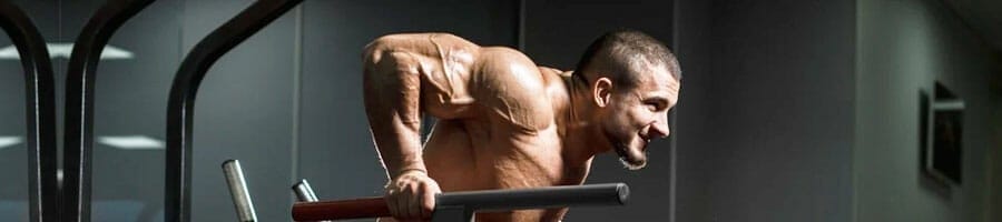 shirtless buff man doing tricep dips inside a gym