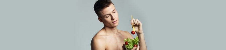 shirtless man devouring a bowl of salad