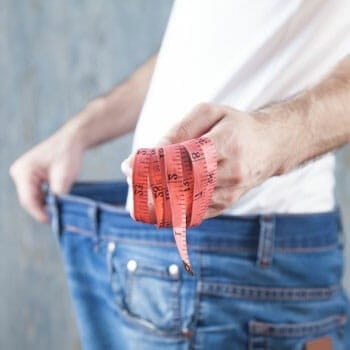man showing a tape measure while holding his loose jeans