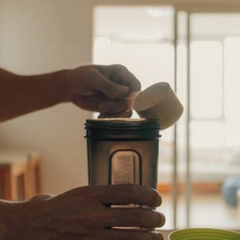 person pouring protein powder in a tumbler