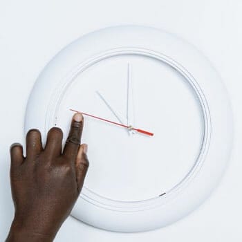 white clock and a hand pointing at it