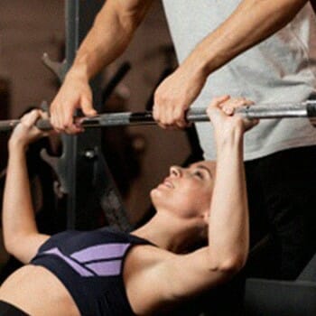 A personal trainer 'Spotting' to help the person lifting the weights