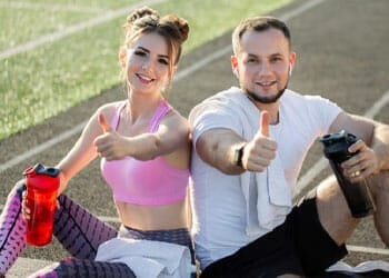 man and woman giving a thumbs up wearing workout clothes