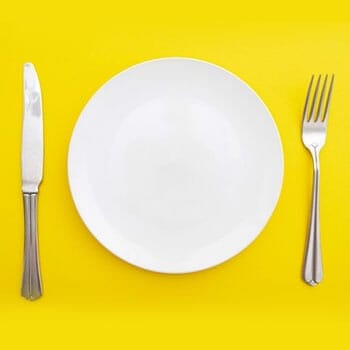 white plate, fork and knife in a yellow background