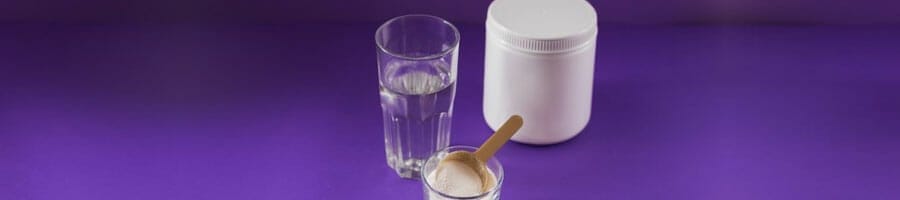 protein powder and a glass of water in a purple background