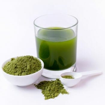 still shot of a green juice, powder and spoon