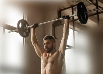 shirtless man lifting a barbell over head
