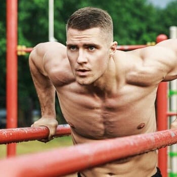 shirtless man doing chest dips in a park