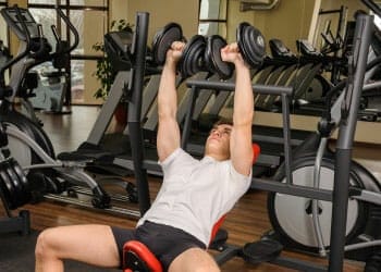 man in a dumbbell press position in a gym