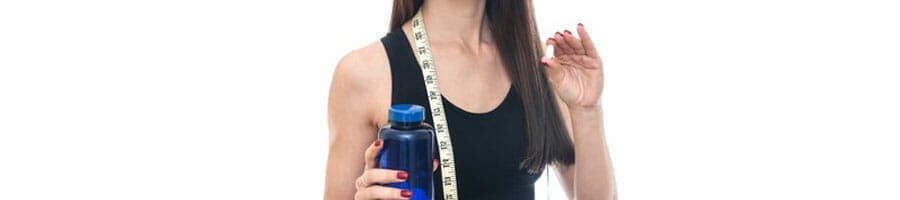 woman holding a pill and container, while a measuring tape is on her