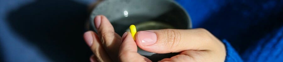 woman holding a cup of water and a yellow pill in one hand