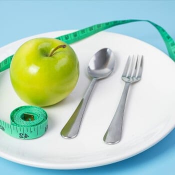 green apple, spoon and fork, and a measuring tape on a plate