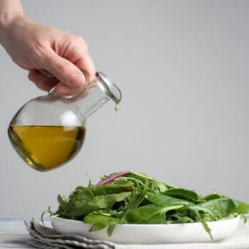 leafy salad bowl getting drizzled by olive oil