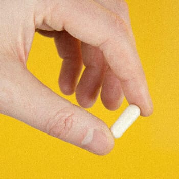 A hand holding a single pill
