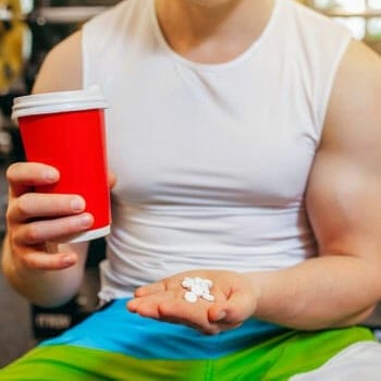 man in a gym holding a drink in one hand and holding a stack of pills on the other