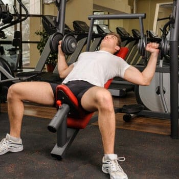 man seated in an incline dumbbell press lifting dumbbells
