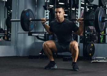 man using a barbell while squatting