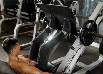 shirtless man using a leg press machine in a gym