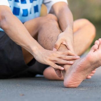 person barefoot holding his calf in pain