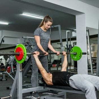 man doing a bench press and a woman assisting him