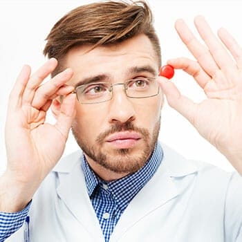 medical person holding up a pill while looking at it