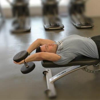 man in a dumbbell pullover position in a gym