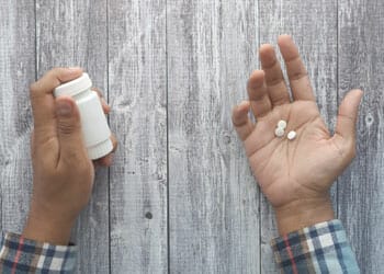 a person's hand filled with white pills and another with pill bottle
