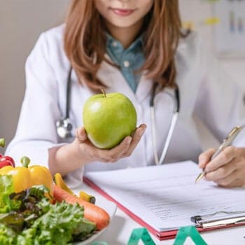 a nutritionist writing on a paper while holding up an apple