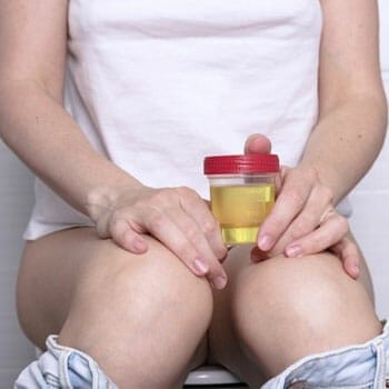 woman peeing in a toilet bowl while holding a container filled with pee