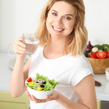 woman holding up a glass of water and a salad bowl