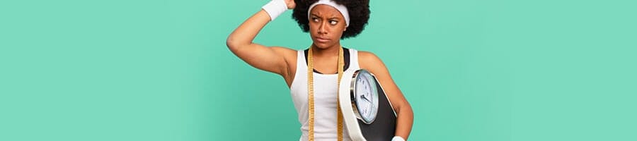 black woman in gym clothes with measuring tape on her neck and holding a scale thinking