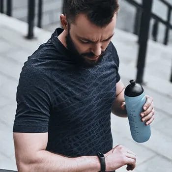 man outdoors looking at his watch and holding a tumbler