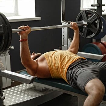 man using a bench to do a barbell press in a gym