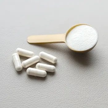spoon filled with white powder and capsules scattered on table