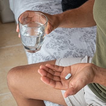 man holding a pill in one hand and a glass of water in his other hand