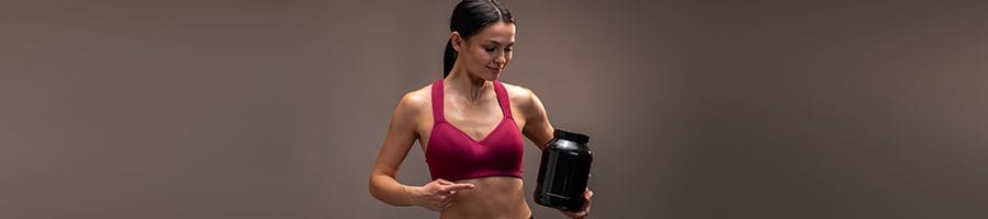 woman holding up a preworkout powder supplement in gym clothes