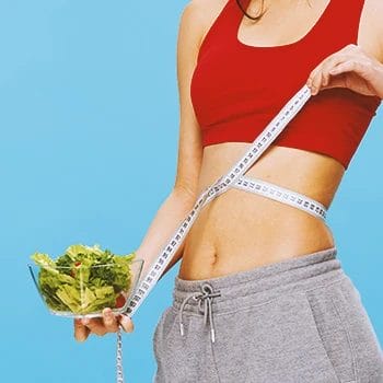 A fit person holding a salad bowl with a measuring tape around her stomach area