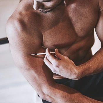 A buff person using a syringe on his biceps