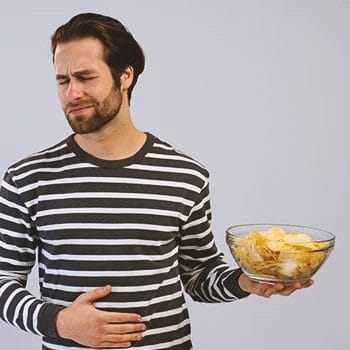 A person holding a bowl of chips while holding his stomach