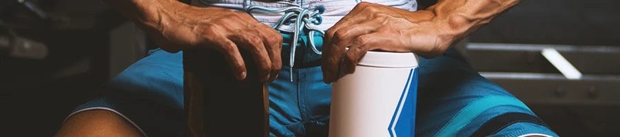 A buff individual holding two tumblers in the gym