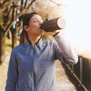 A person drinking from a tumbler outside in a park
