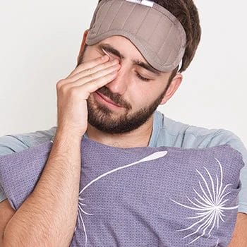 A man scratching his eye while holding a pillow