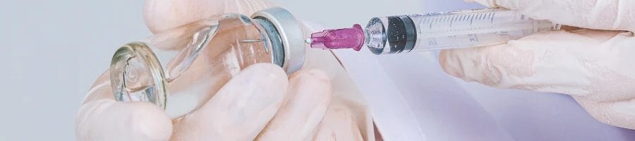 A person injecting a syringe into a bottle