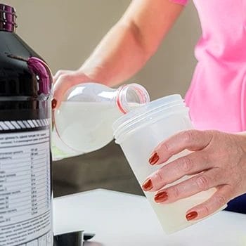 Woman pouring energy drink inside tumbler with pre workout supplement