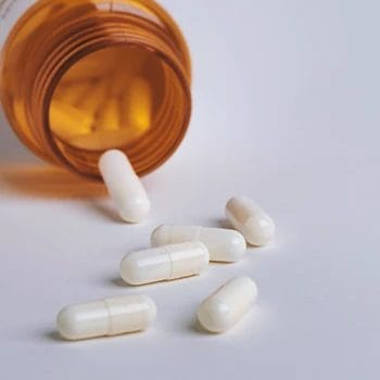 A bunch of white pills spilled on a white table from an orange bottle