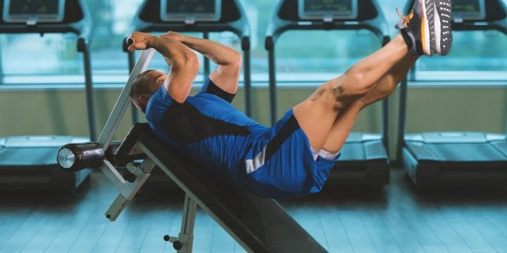 A buff man working out his abs on a bench in the gym