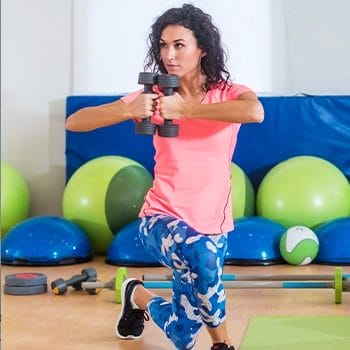 Woman holding dumbbell while performing curtsy lunge