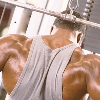 A buff male in the gym doing behind the neck pulldowns
